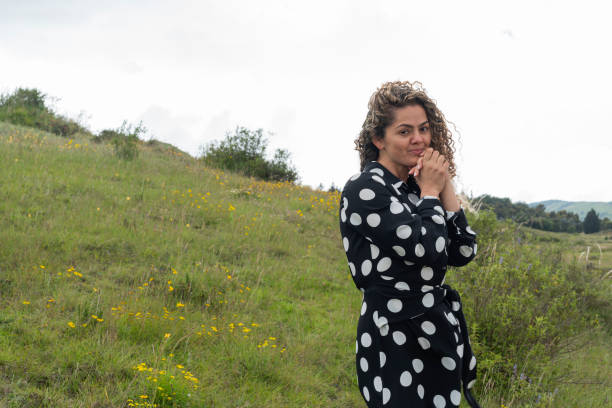 Average 35-year-old curly-haired Latin woman dressed in a black dress with white balls walks with great enthusiasm through a desert surrounded by nature enjoying the walk and nature while looking at the camera