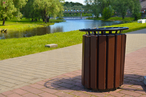 Brown wooden trash can on the street on the riverbank in the park. Garbage container outside.