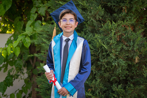 Teenage boy wearing cap and gown holding diploma in schoolyard