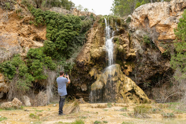 istock Standing man photographing a waterfall with his smartphone. 1408744063