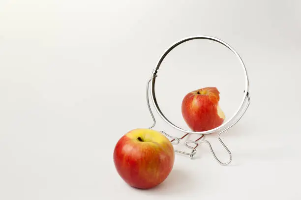 A fresh red apple is reflected as a bitten apple in the mirror