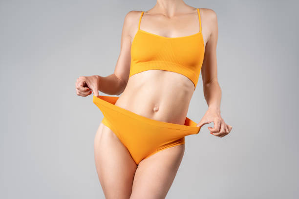 Slim woman in yellow underwear after weight loss on gray background stock photo