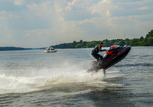 06-09-2013  Moscow Oblast. Russia. A  strong man rides a jet ski on a lake on a summer day-  splashes fly in all directions  in the  sun !  Background - lake  , forest   and motoryacht.