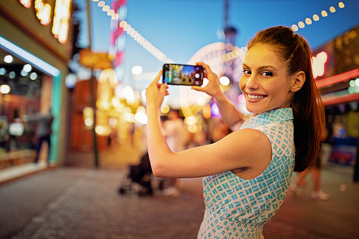 Happy young woman is taking pictures in a fun fair