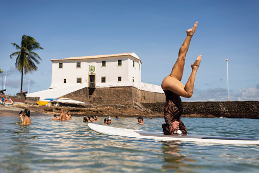 Salvador, Bahia, Brazil - June 04, 2022: Woman stands upside down on a surfboard at Porto da Barra beach in Salvador, Bahia.