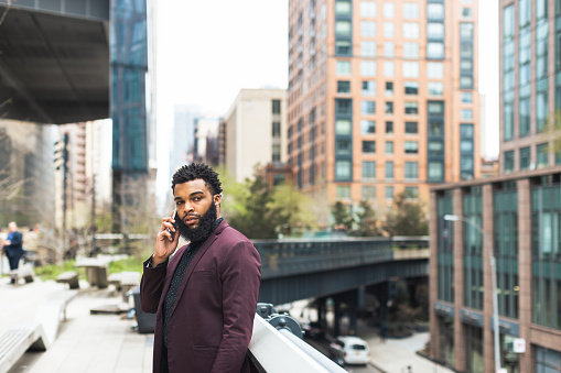 Black businessman walking to the office and having phone call in front of the office building. Hudson Yards, New York City, USA