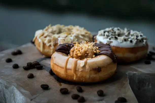 Three doughnuts covered with Choco peanut butter, Cookies and creme and Almendras on wooden cutting board. The concept of delicious glazed donuts, Space for text, Selective Focus.