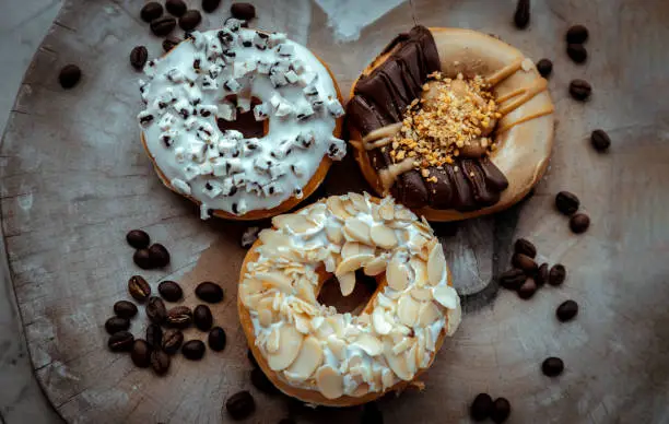 Three doughnuts covered with Cookies and creme, Almendras and Choco peanut butter on wooden cutting board. The concept of delicious glazed donuts, Top view, Selective Focus.