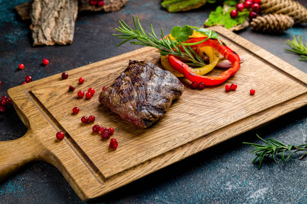 istock Venison steak with sliced vegetables on the board on dark table 1408774719