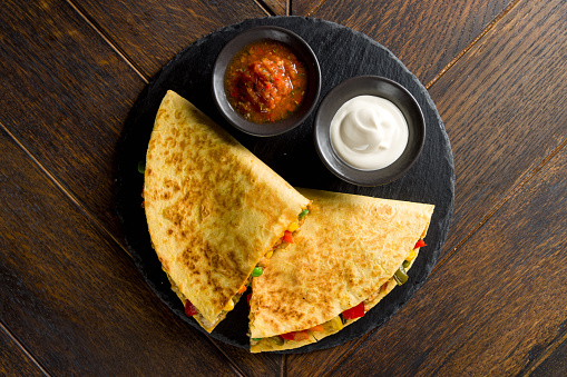 Mexican Quesadilla with chicken, vegetables, cheese and sauces on black stone plate