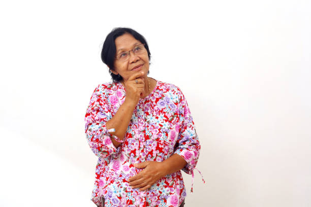 An elderly Asian woman looking at the camera with a smile while sitting on a chair on a white background