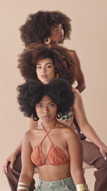 Group of beautiful diverse females only with afros posing in the studio. Three powerful diverse women with afros sitting behind each other, shifting focus