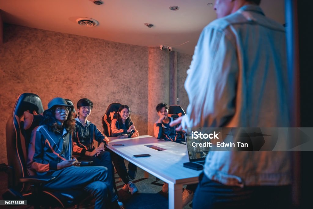 Asian Esport Team listening to Coach analysing briefing strategy before grand final videogame competition in meeting room Gaming Chair Stock Photo