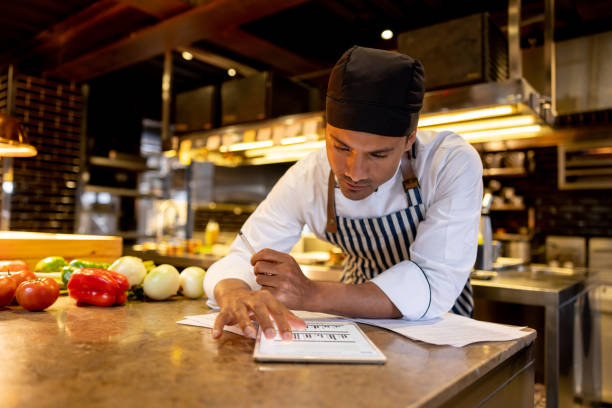 Cook working at a restaurant and looking at a recipe online Latin American cook working at a restaurant and looking at a recipe online using a tablet computer - food service concepts commercial kitchen photos stock pictures, royalty-free photos & images