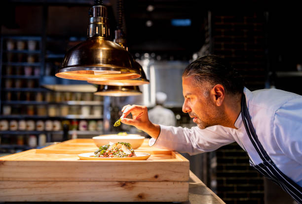 chef decorando un plato mientras trabaja en la cocina de un restaurante - chef fotografías e imágenes de stock