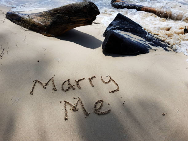 The words Marry Me and Hearts written on sandy beach