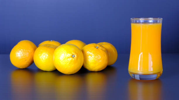 стакан апельсинового сока и группа свежих апельсинов на черном фоне. - orange black horizontal saturated color стоковые фото и изображения