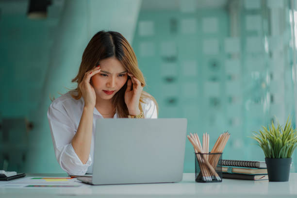 istock Asian businesswoman having a headache during work analyzing financial graphs with laptop at office desk 1408802617