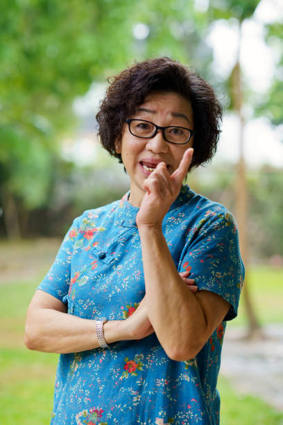Portrait of serious senior Asian woman talking and pointing finger, looking at the camera.