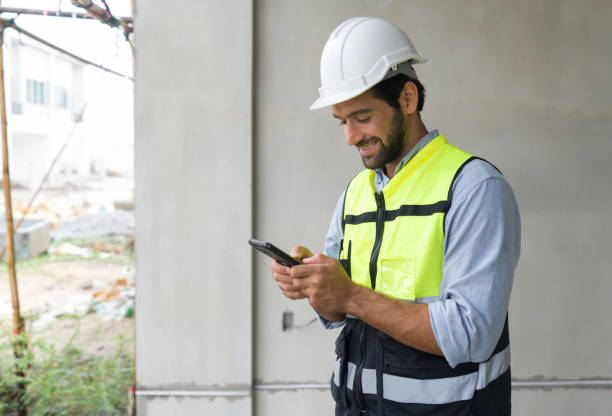 istock Young engineer in hardhat and safety vest typing text massage on mobile phone. Work environment of engineers at the construction site. 1408804183