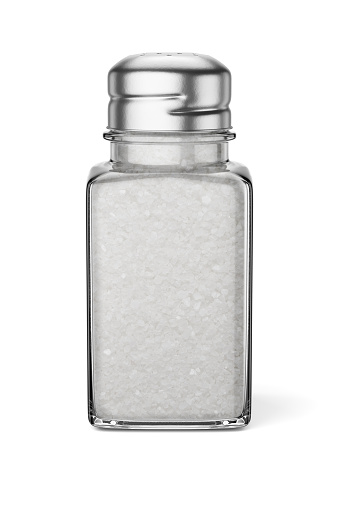 Salt. Glass salt shaker on dark stone table.  A pile of salt top view.