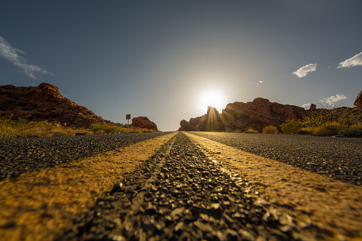 In Valley of Fire the road is running through the hot red rock desert landscape. Seen in Nevada, USA, a hot day at sunset from a cat perspective.