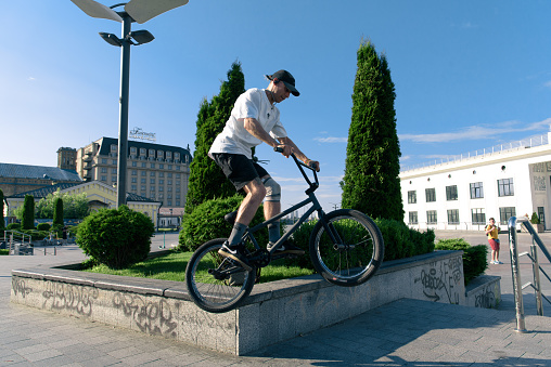 Kyiv, Ukraine - June 15, 2022: Contract Square. Bmx biker performing tricks and stunts training in city park. Jump on bmx bike in action