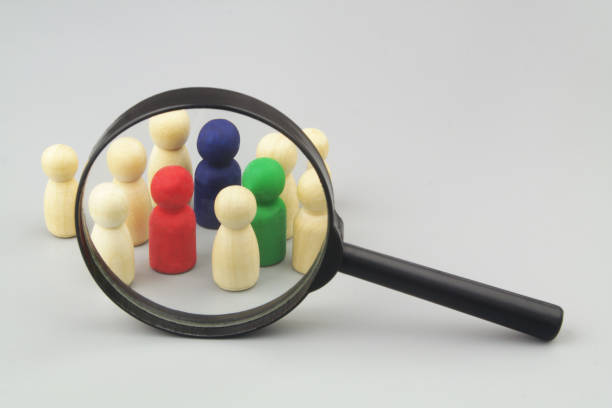 istock Group of not colored figures with few colored under magnifying glass on grey background. 1408818097