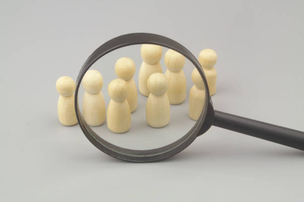 istock Wooden figures and magnifying glass on grey background. 1408818098