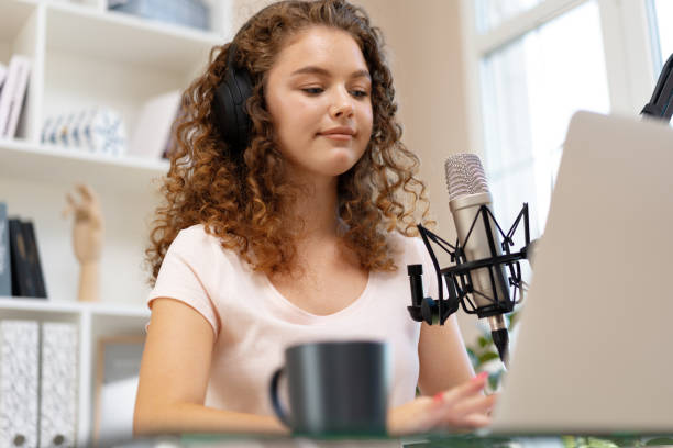 istock Young curly female recording podcast from home and talking into a microphone 1408820111