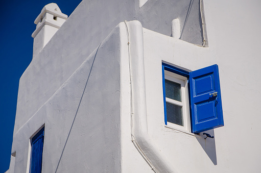 Traditional greek architecture in a narrow alley in Skiathos town, Sporades archipelago, Greece with cobblestone pathways, blue painted windows, door and furniture, whitewashed walls and beautiful bougainvillea in full bloom. All signs are edited except the one that says \