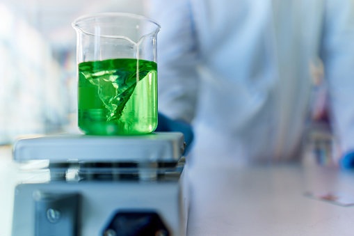 Close up of green liquid in a beaker while heating on a magnetic stirrer in laboratory.