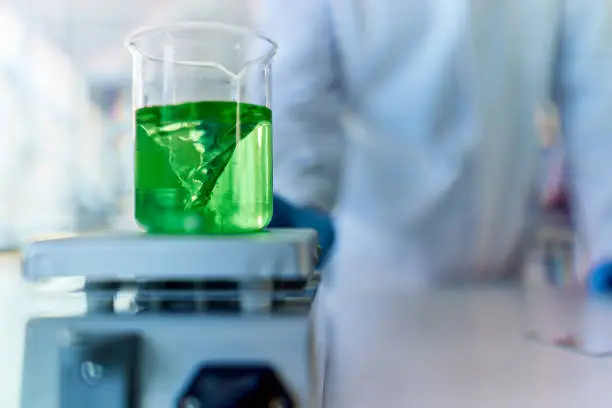 Close up of green liquid in a beaker while heating on a magnetic stirrer in laboratory.