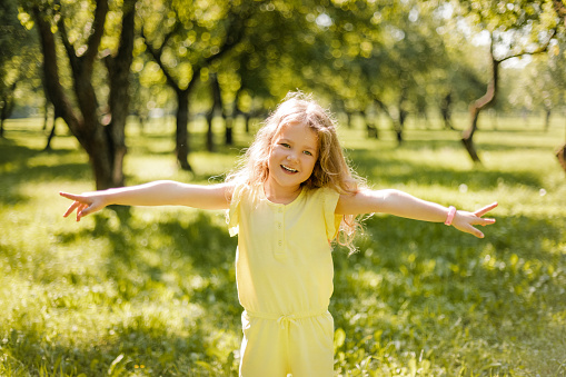 A happy child playing in a summer park. The girl is running, spinning, spinning and laughing. Entertainment during the summer holidays.