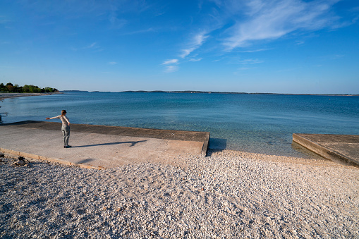 Back view of senior woman exercising on the beach in spring. Shi is in small place Peroj near Pula in Istria, Croatia with Brioni islands in horizon.