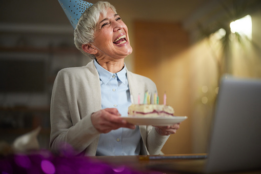 Happy senior woman having fun while celebrating her Birthday with someone through video call at home.