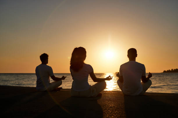 istock Back view of athletic people meditating on the beach at sunset. 1408837770