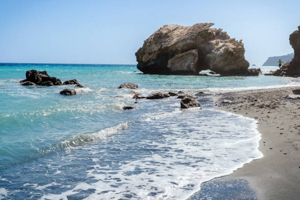 istock Hypnotic seascape view with gray sand and beautiful cliffs in very quiet and remote Tertsa beach. Young man runs to climb high rock. Myrtos village, Lassithi prefecture, Crete island, Greece. 1408837955