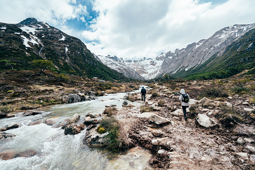 Ushuaia, Argentina - November 17, 2019: Two people doing a trekking near Río Lasifashaj in Patagonia, Tierra del Fuego, Argentina. Also know as Rio Larsiparsahk. The photo is taken near Laguna Esmeralda, a lake close to Ushuaia.
