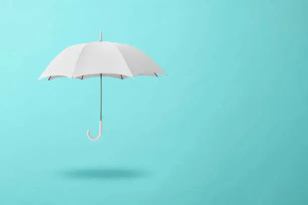 White umbrella floating in mid-air against light blue background with copy space.