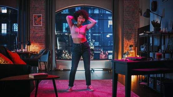 Portrait of Diverse Multiethnic Young Latin Female Dancing in Futuristic Neon Glowing Glasses, Having a Party at Home in Loft Apartment. Recording Funny Viral Videos for Social Media.