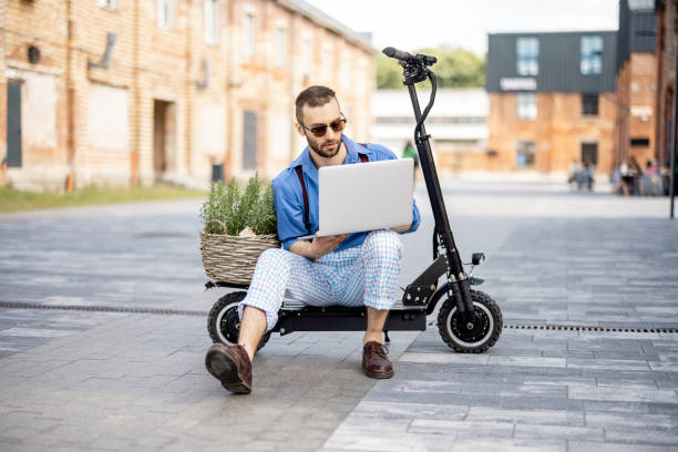 istock Man works on laptop while sitting on electric scooter outdoors 1408843734