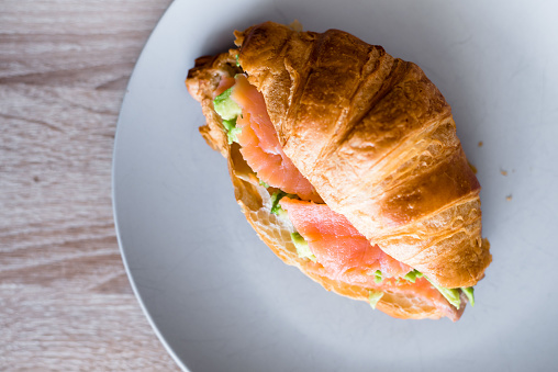 Fresh croissant with salmon and avocado. Healthy and tasty breakfast. Healthy diet. Close-up.