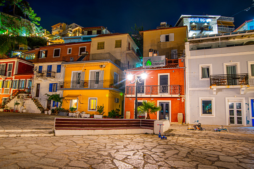 06 June 2022, PARGA, GREECE, the amazing coastal city of Parga at night with unsharp, motion blurred tourists and visitors walk across the coast next to the beautiful, decorated shops, and restaurants. Parga, Epirus, Greece, Europe.