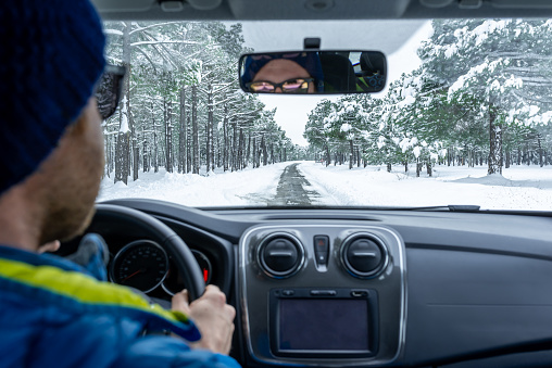 View of a blurred young man driving a car on a snow covered road through a idyllic snowy pine forest. Winter wonderland.