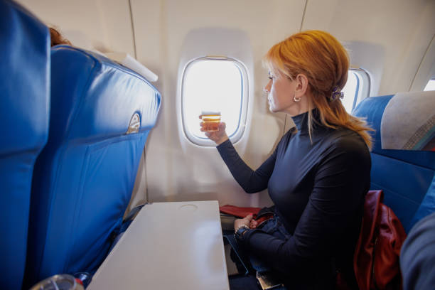 istock Woman having a drink on the airplane and looking through window 1408855048