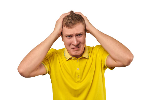 Upset man in yellow T-shirt clutched at his head, forgetful man with headache isolated on white background. Young guy worried and frustrated, grabbed his head, sharp severe headache