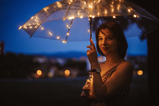 Beautiful young woman holding an umbrella with lights at night.