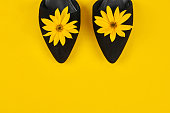 Suede black court shoes with yellow Topinambur flower bud on yellow background, womanhood concept