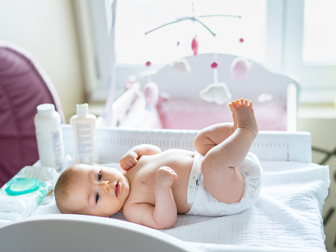 Cute baby girl in diaper on changing table at home